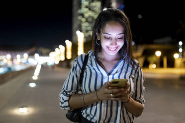 Smiling young woman text messaging through mobile phone at night - WPEF06352