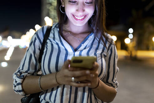 Glückliche Frau, die nachts über ihr Smartphone im Internet surft - WPEF06353