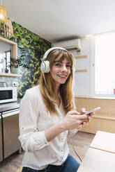 Happy businesswoman with mobile phone sitting in cafeteria - PNAF04468