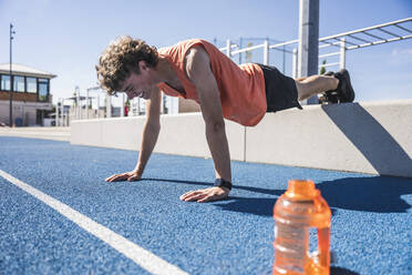 Happy sportsman doing push-ups on running track - UUF27147