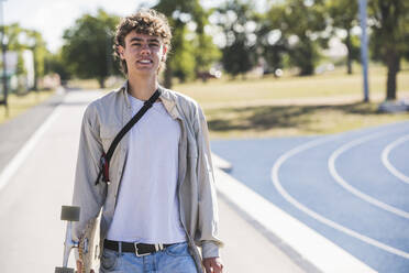 Smiling young man with skateboard on footpath - UUF27169