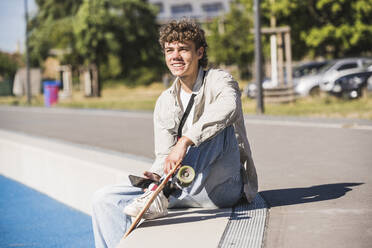 Glücklicher Mann mit Skateboard und Smartphone am Rande der Bahn - UUF27175