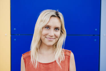 Smiling young woman with blond hair in front of colorful wall - EBBF05959