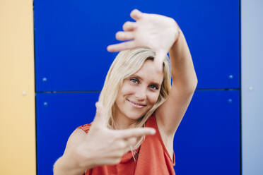 Smiling woman gesturing finger frame in front of colorful wall - EBBF05961