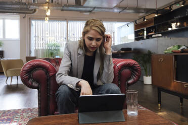 Junge Frau sitzt im Sessel und arbeitet an einem digitalen Tablet - WESTF24984