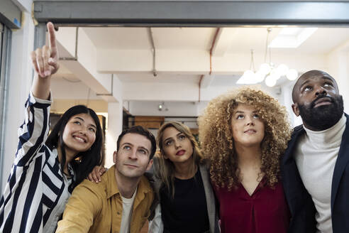 Curious young business people standing in office looking up - WESTF24990