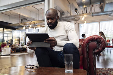 Confident businessman sitting in armchair using digital tablet - WESTF25027