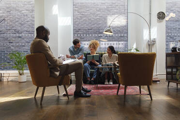 Geschäftsleute, die in einem modernen Coworking Space sitzen und gemeinsam Brainstorming betreiben - WESTF25036
