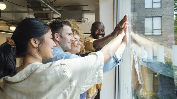 Group of business people looking out of window stacking hands - WESTF25059