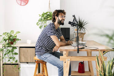 Mann sitzt auf einem Hocker und nimmt einen Podcast im Heimstudio auf - XLGF03045
