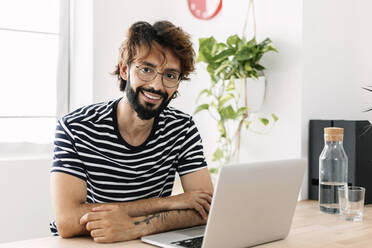 Happy man sitting with laptop at home office - XLGF03054