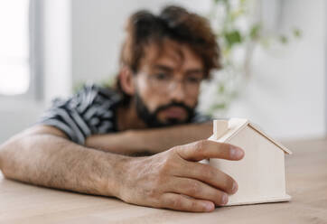 Mann mit kleinem Modellhaus zu Hause sitzend - XLGF03064