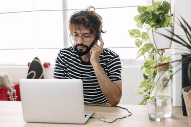 Freiberufler mit Kopfhörern bei der Arbeit am Laptop im Heimbüro - XLGF03070