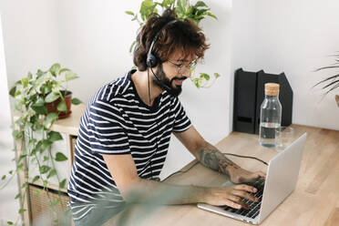 Smiling freelancer using laptop wearing headset in home office - XLGF03071