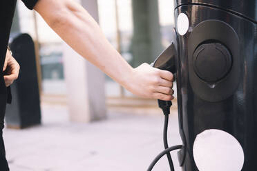 Die Hände eines Mannes, der ein Ladegerät für ein Elektroauto aus einer Stromtankstelle herauszieht - AMWF00365