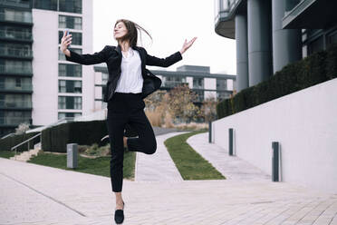 Carefree businesswoman dancing with smart phone outside building - AMWF00378