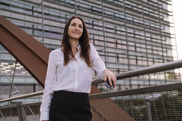 Smiling mature businesswoman standing by railing on bridge - AMWF00383