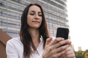 Ältere Geschäftsfrau, die ein Smartphone auf einer Brücke vor einem Gebäude benutzt - AMWF00384