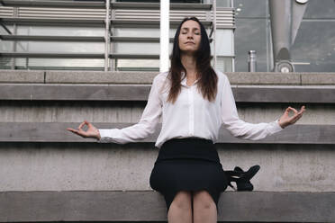 Mature businesswoman meditating on steps outside office building - AMWF00387