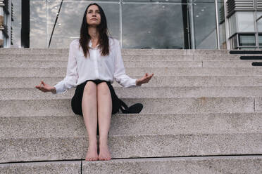 Thoughtful businesswoman doing meditation sitting on steps - AMWF00388