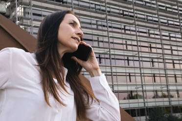 Reife Geschäftsfrau, die vor einem Bürogebäude mit einem Smartphone telefoniert - AMWF00399