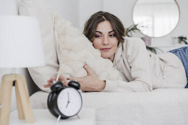 Beautiful woman lying in bed reaching for alarm clock - EBBF05986