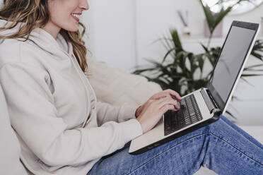 Smiling woman typing on laptop at home - EBBF06011