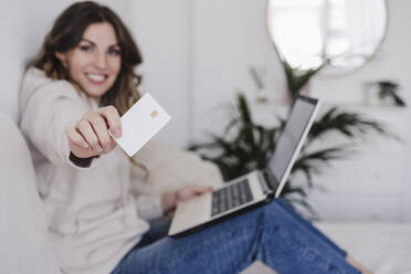 Smiling young woman with laptop showing credit card - EBBF06019