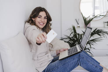 Happy young woman with laptop showing credit card - EBBF06020