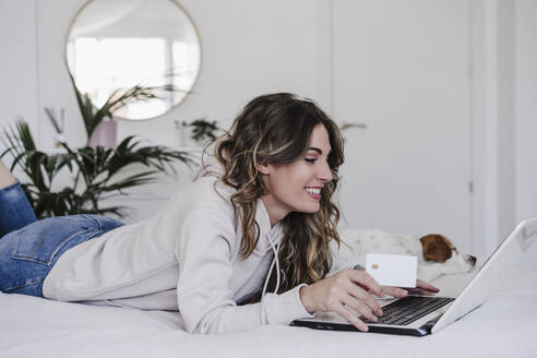 Smiling woman shopping online with credit card lying by dog - EBBF06022