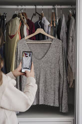 Woman taking picture of top through smart phone hanging in closet - EBBF06030