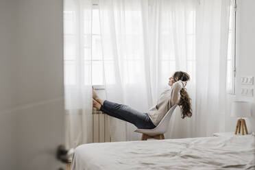 Young woman relaxing in chair at home - EBBF06032