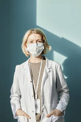 Mature doctor with protective face mask in front of wall - DSHF00506