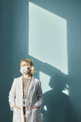 Doctor wearing protective face mask standing in front of wall - DSHF00507