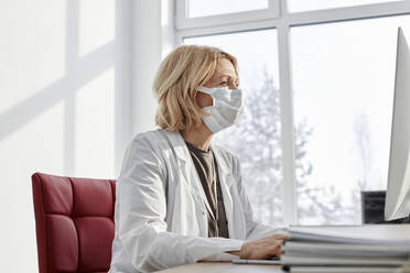 Arzt mit Schutzmaske bei der Arbeit an einem Desktop-PC in einer Klinik - DSHF00512