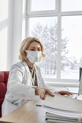 Arzt mit Gesichtsschutzmaske, der eine Akte am Schreibtisch in einer Klinik abholt - DSHF00514