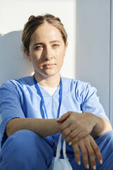 Doctor wearing scrubs resting in front of wall - DSHF00533