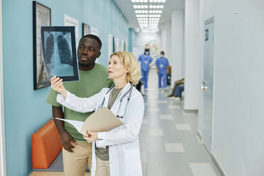 Mature doctor examining X-ray with patient standing in hospital corridor - DSHF00535