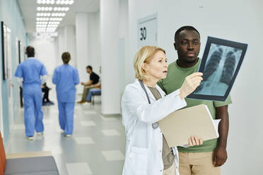 Doctor explaining X-ray image to patient standing in hospital corridor - DSHF00536