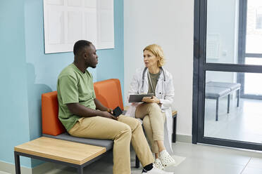 Doctor discussing with patient sitting on couch in clinic - DSHF00541