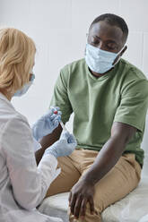 Patient sitting on bed with doctor preparing vaccine syringe in clinic - DSHF00559