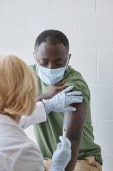 Doctor injecting COVID-19 vaccine on patient arm in clinic - DSHF00560