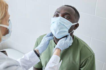 Doctor checking neck of patient wearing protective face mask in clinic - DSHF00565