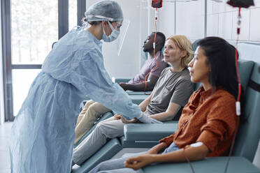 Frau, die Blut spendet, im Gespräch mit einer Krankenschwester mit Gesichtsschutz in einer Klinik - DSHF00571