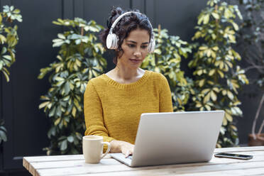 Geschäftsfrau hört Musik über Kopfhörer bei der Arbeit am Laptop im Café - JSRF02195