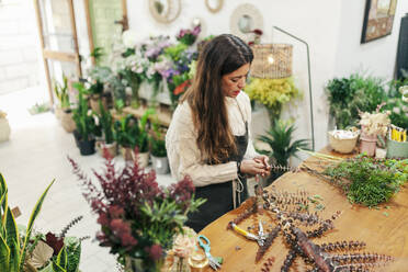 Saleswoman arranging leaves on workbench at floral shop - MRRF02406