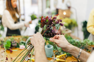 Hände eines Blumenhändlers beim Binden von Pflanzen im Blumenladen - MRRF02414