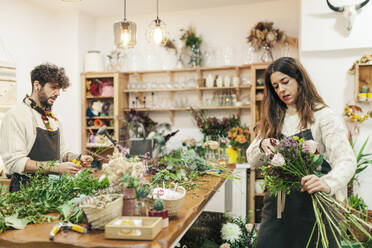 Verkäuferin, die in einem Blumenladen einen Blumenstrauß von einem Kollegen anfertigt - MRRF02417