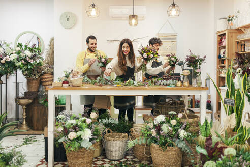 Colleagues making bouquet standing by workbench at flower shop - MRRF02422