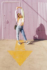 Woman with arms raised standing on arrow symbol in front of corrugated wall - MGRF00745